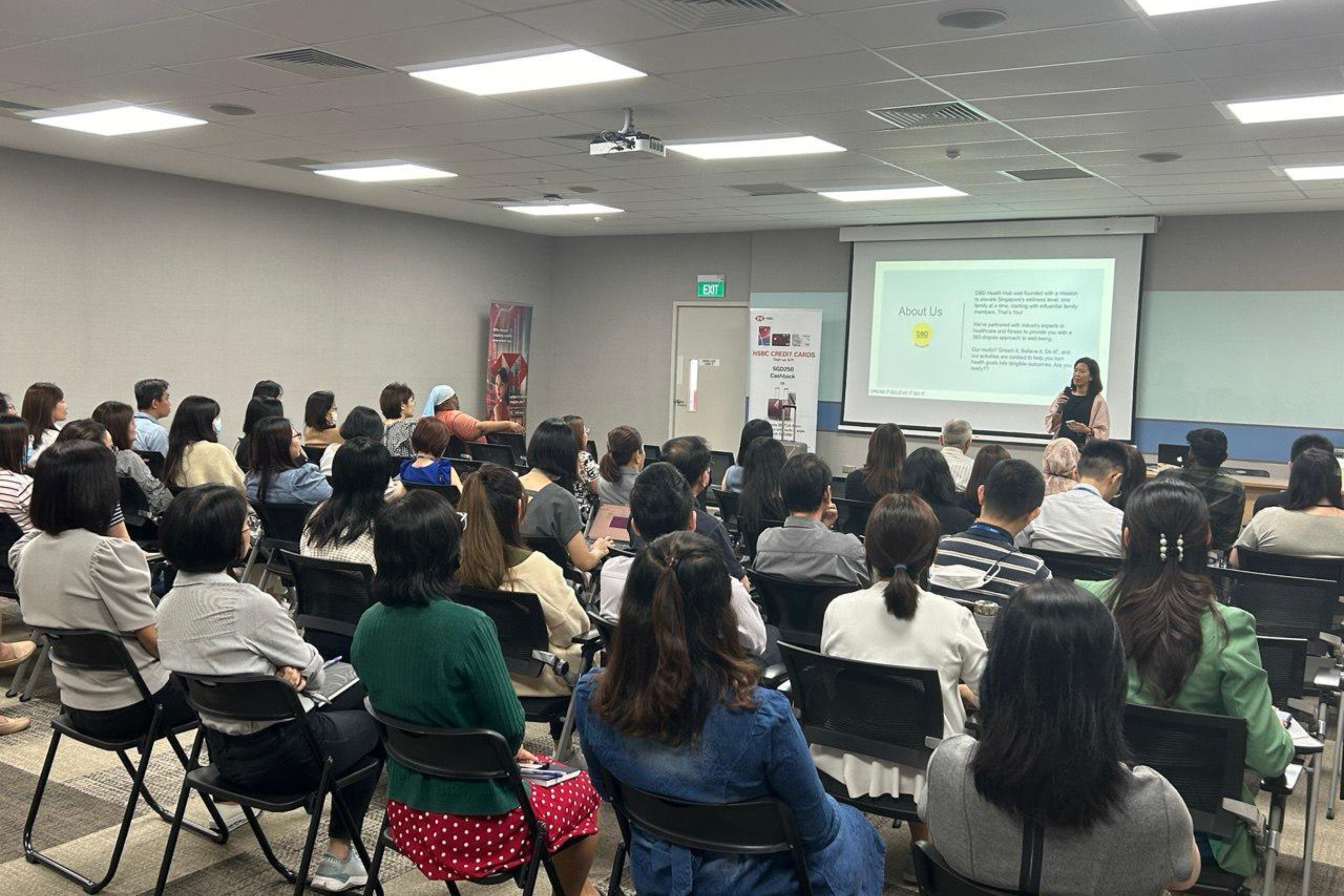 DBD HUB corporate wellness health talk session in Singapore with an employee group attending a mental wellness workshop led by a female speaker, promoting workplace wellness, employee wellbeing, and preventive care programmes.