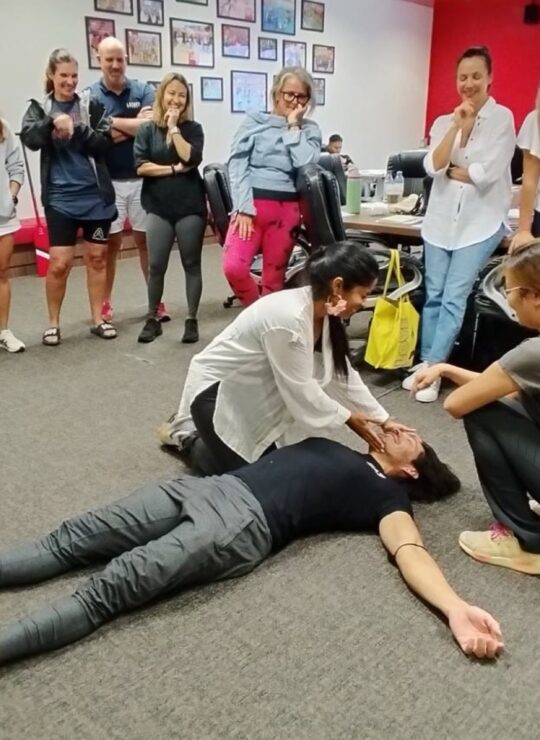DBD HUB corporate wellness certified first aid training session in Singapore with a trainer demonstrating life-saving techniques while employees watch to learn CPR and emergency response skills for workplace safety.